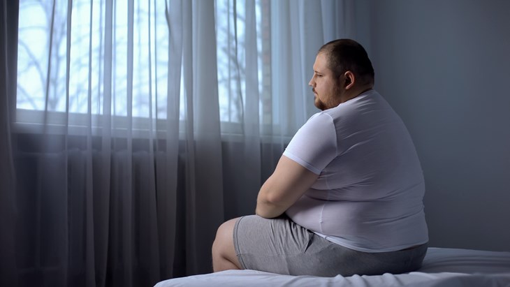 Overweight unhappy man sitting on a bed