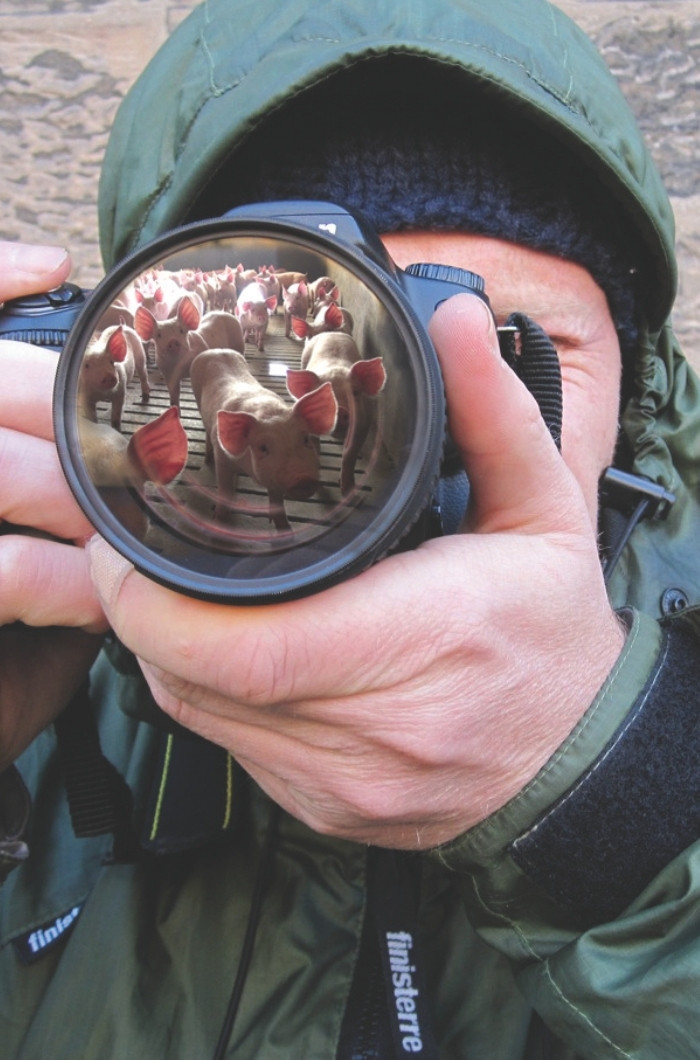 Un homme avec une capuche relevée tenant une caméra devant son visage.